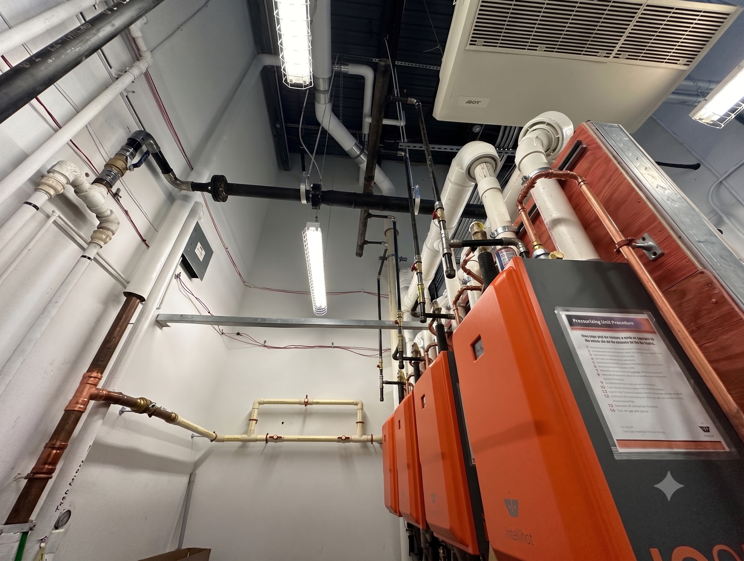 Commercial boiler plant with condensing boilers, copper supply mains, PVC flue venting, and hydronic piping in a mechanical room