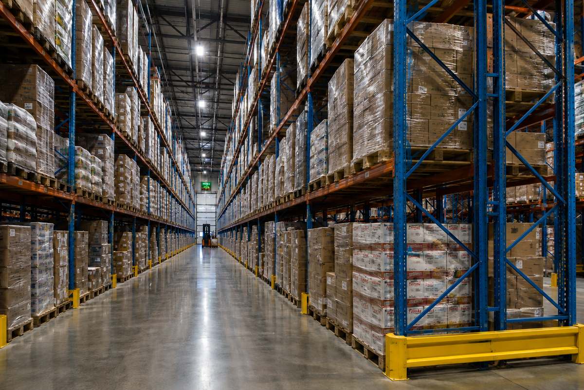 Large modern cold-storage and distribution warehouse interior with tall steel racking, insulated panel walls, and a forklift in a wide aisle